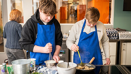 Leerlingen staan in de keuken en bakken vlees in een pan.