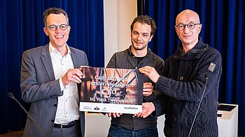 Wethouder Hans van Daalen en projectleider Jochem Damhuis (midden) reiken de cheque uit aan deelnemer Mark Holmwood (rechts)  