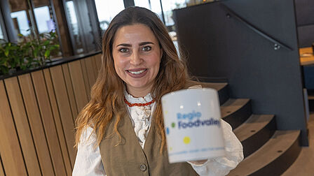 Lianne Schonewille van ION Vallei houdt de koffiemok van Regio Foodvalley vast. Ze houdt deze omhoog. 