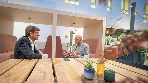 Jan Hol en Pieter Oudenaar zitten aan een tafel en zijn in gesprek.