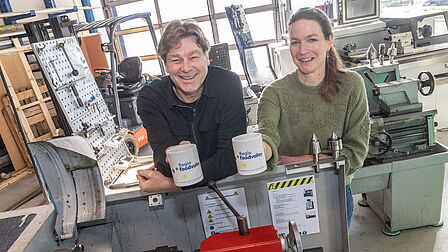Annet Leeflang en Hans Schipper van Technova College staan in de werkplaat met de koffiebeker.