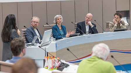 De sprekers zitten achter een desk voor het beantwoorden van vragen uit het publiek.