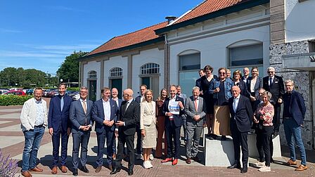 Groepsfoto van de deelnemers aan het werkbezoek in Nijkerk. De deelnemers staan voor het stationsgebouw. 