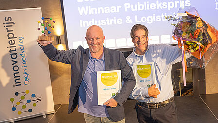 De heren van WEMO-techniek staan juichend met de prijs en bloemen in de hand. 