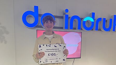 Krijn uit Ede wint de aanmoedigingsprijs van 100 euro. Hij houdt een cheque vast.