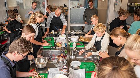 Overzichtsfoto van de leerlingen Van Lodenstein College in de keuken. Iedereeen is druk aan de slag. 