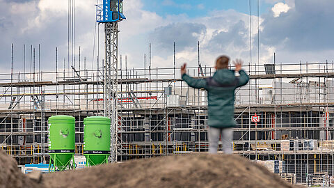 Een jongen staat op een zandheuvel en kijkt een een bouwproject waar nieuwe woningen worden gebouwd. 