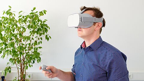 een man heeft een virtual reality-bril op. Hij staat in een kantoor. 