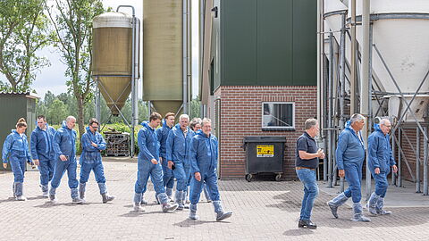 De deelnemers lopen op de boerderij in beschermende pakken. 