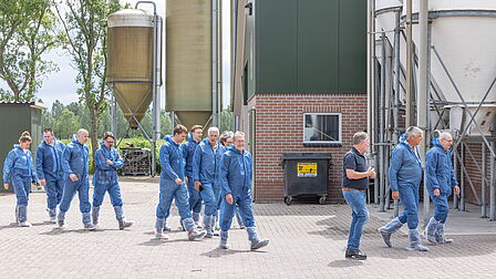 De deelnemers lopen op de boerderij in beschermende pakken. 
