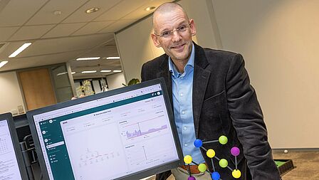Directeur Dik Geelen van Unica Energy staat bij de computer. Er staan statistieken op het beeldscherm. Op het bureau staat de award van de Innovatieprijs Regio Foodvalley.