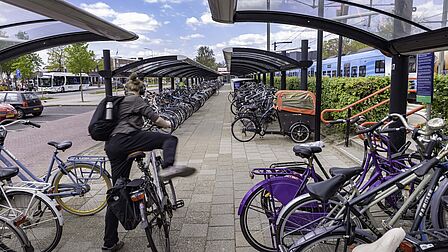 Fietsenstalling bij station Barneveld Centrum. Een jonge dame stapt op de fiets en de Valleilijn rijdt weg. 